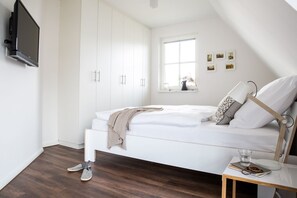 A bedroom with a bed, a bedside table, a TV mounted on the wall, and a window with pictures on the wall.