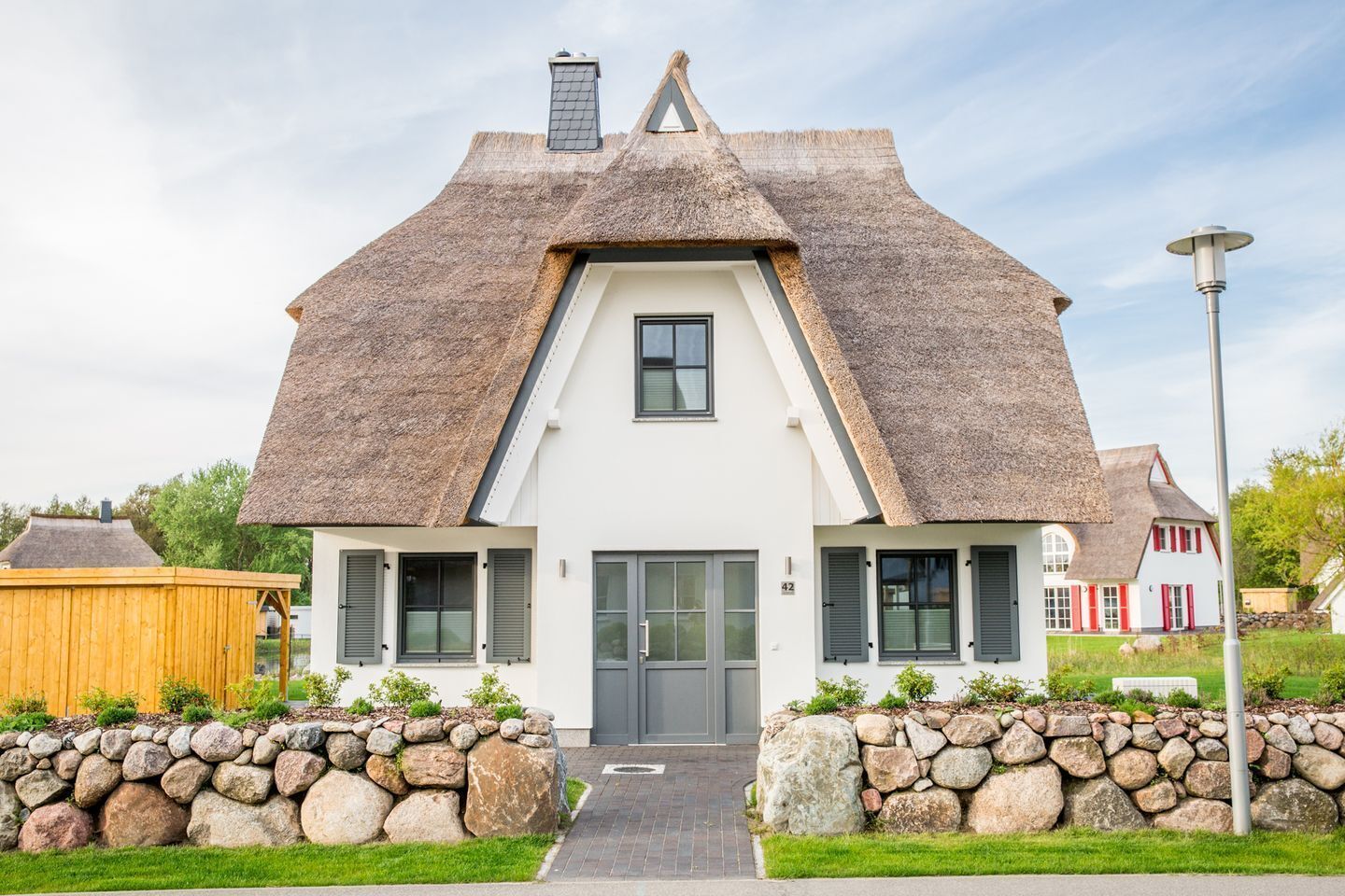 A house with a steeply pitched roof, a central entrance, and a stone wall in front.