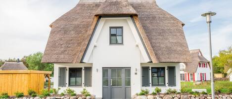 A house with a steeply pitched roof, a central entrance, and a stone wall in front.