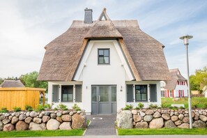 Een huis met een steil dak, een centrale ingang en een stenen muur ervoor.
