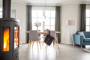 A modern living room with a wood-burning stove, a dining area with chairs and a table, and a blue sofa.