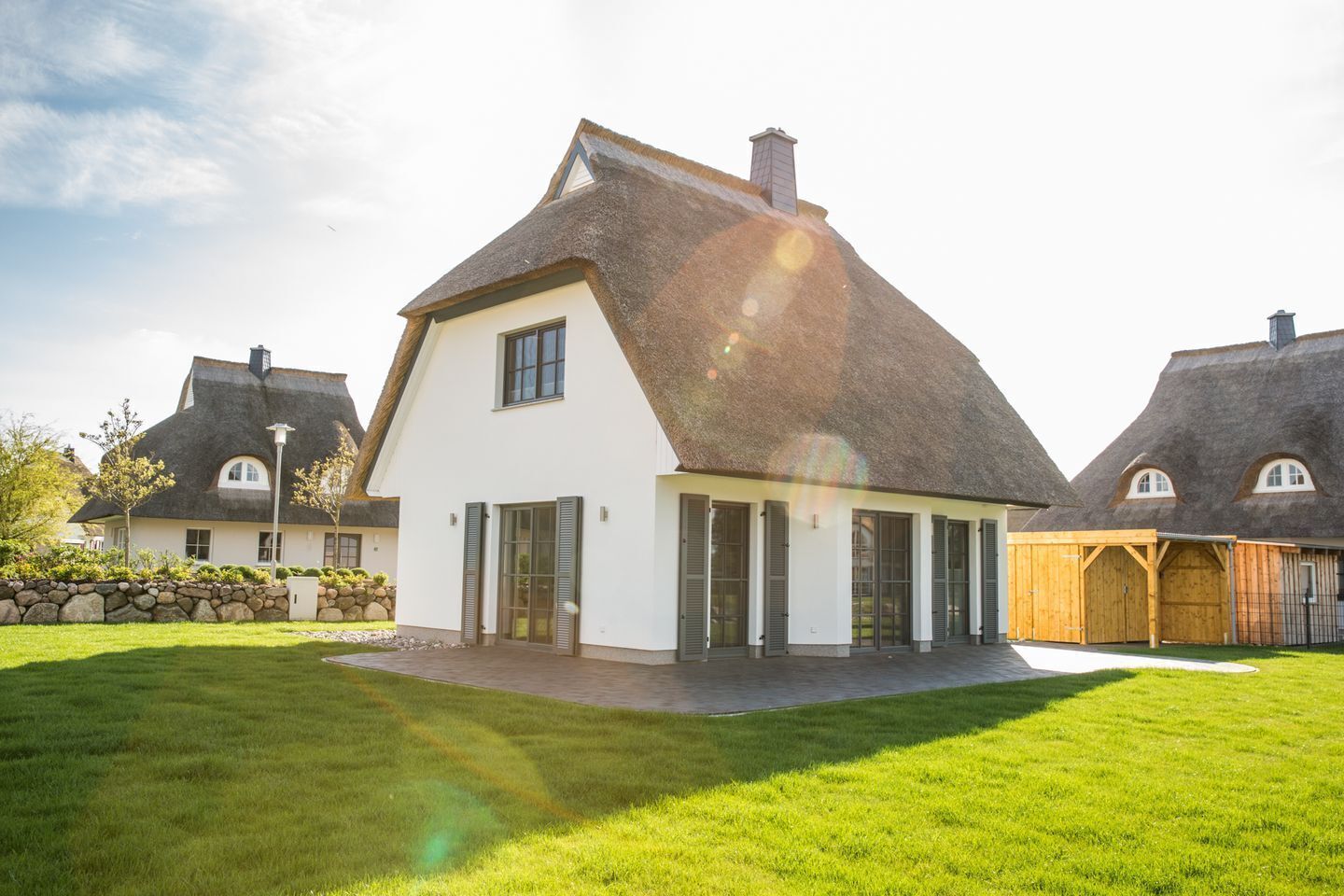 A modern house with a white exterior, a steeply pitched roof, and a stone wall surrounding the property.