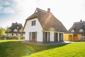 A modern house with a white exterior, a steeply pitched roof, and a stone wall surrounding the property. - Vacation home Seeschwalbe 33 - Holiday home Seeschwalbe 33 - Close to nature (Fuhlendorf)
