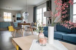 A modern living room with a wooden table, a vase with flowers, and a blue sofa. - Vacation home Seeschwalbe 33 - Holiday home Seeschwalbe 33 - Close to nature (Fuhlendorf)