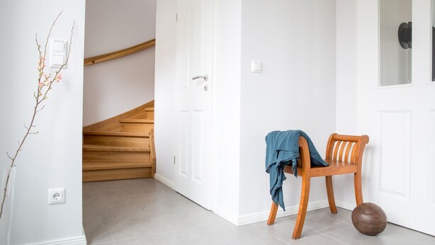 A hallway with a wooden staircase, a white door, and a wooden chair with a ball. - Vacation home Seeschwalbe 33 - Holiday home Seeschwalbe 33 - Close to nature (Fuhlendorf)