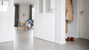 A modern living room with a sofa and a chair, a coat rack with a coat and shoes, and a door leading to another room. - Vacation home Seeschwalbe 33 - Holiday home Seeschwalbe 33 - Close to nature (Fuhlendorf)