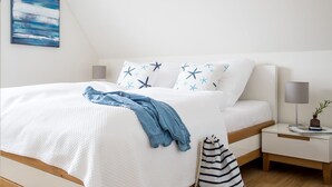 A neatly made bed with a white and blue star-patterned pillow, a denim blanket, and a striped bag on the floor. - Vacation home Seeschwalbe 33 - Holiday home Seeschwalbe 33 - Close to nature (Fuhlendorf)