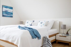 A neatly made bed with a white and blue star-patterned pillow, a denim blanket, and a striped bag on the floor. - Vacation home Seeschwalbe 33 - Holiday home Seeschwalbe 33 - Close to nature (Fuhlendorf)