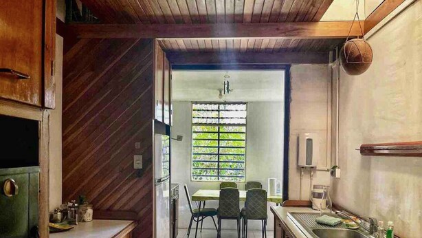 A compact kitchen with wooden cabinets, a dining area with chairs, and a window with blinds. - Peaceful Home (Desamparados)