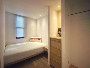A small, neatly arranged bedroom with a single bed, a dresser, and a window with blinds.