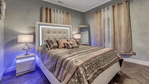 A bedroom with a tufted headboard, a bedside table with a lamp, and patterned bedding. - 💎Urban Glam Gem💎 Rancher near Gonzaga w/GiG Internet (Spokane)