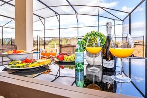 A table with food, drinks, and a glass of wine on a balcony with a glass enclosure and a view of the landscape. - Magnificent 12bd House Perfect for Family Gatherings, Close to Disney #12st8029 (Davenport)