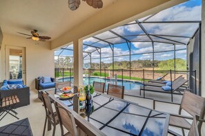 A spacious outdoor area with a glass-enclosed pool, lounge chairs, and a dining table with outdoor seating. - Magnificent 12bd House Perfect for Family Gatherings, Close to Disney #12st8029 (Davenport)