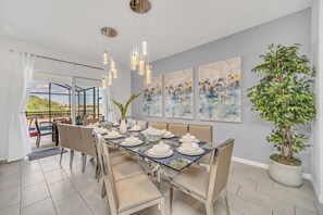 Un comedor moderno con una mesa de vidrio, sillas color beige y una planta grande en maceta.