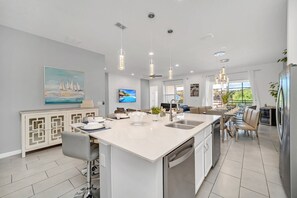 Una cocina moderna con una isla grande, muebles blancos y un comedor con vistas al exterior.