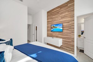 A modern hotel room with a wooden accent wall, a bed with blue bedding, a TV mounted on the wall, and a white cabinet below. - Magnificent 12bd House Perfect for Family Gatherings, Close to Disney #12st8029 (Davenport)
