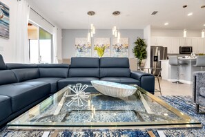 Una sala de estar moderna con un sofá modular, una mesa de centro de vidrio y una cocina al fondo.
