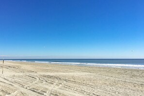 Uma praia com marcas de pneus visíveis e um céu azul límpido.