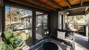 A covered porch with a wooden ceiling, large windows, and outdoor seating. - Heavensent Tiny Home @ The Retreat at Water's Edge - Lake Views! (Tracy City)