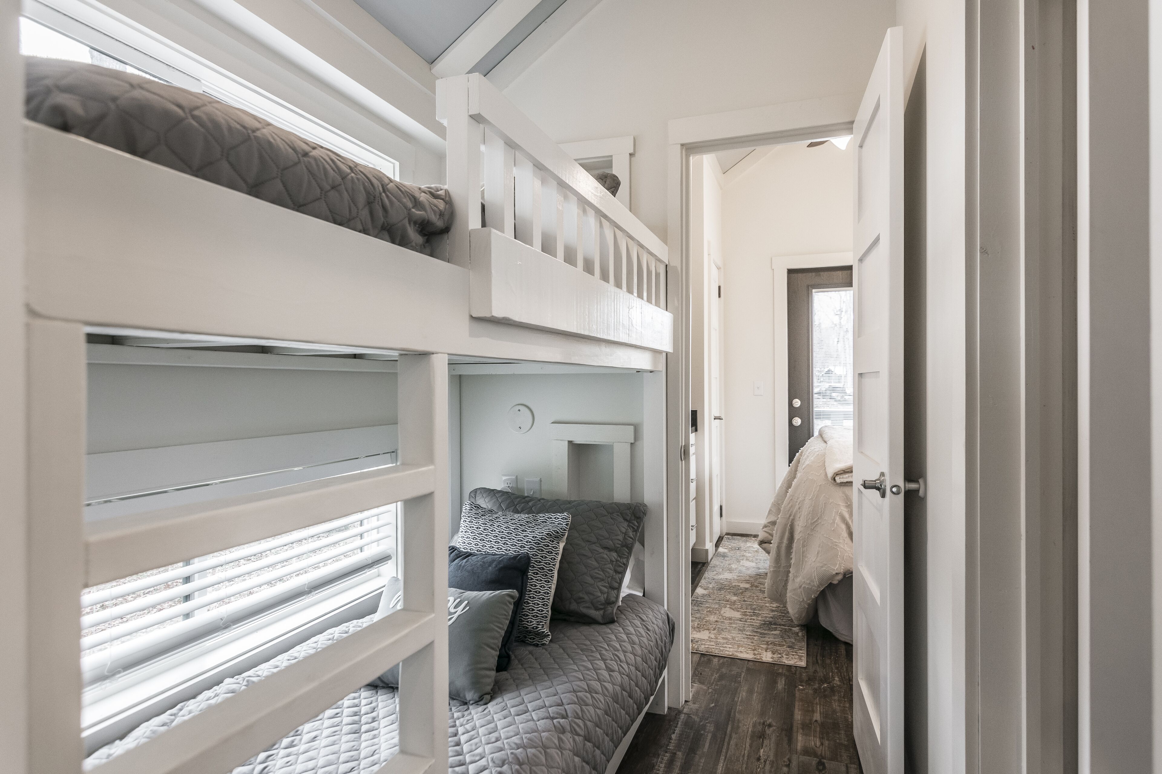 Habitación con literas, una pequeña mesa de escritorio y una puerta que da a otra habitación.