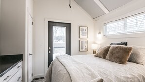 A bedroom with a bed, a door, a window, and a wall-mounted light fixture. - Heavensent Tiny Home @ The Retreat at Water's Edge - Lake Views! (Tracy City)