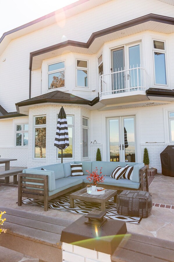 A two-story house with a covered patio area featuring a light blue sofa, a wooden bench, and a small table with a tray. - 🏔Views for Days! Welcome to the Missoula Lookout! 🏔 (Missoula)