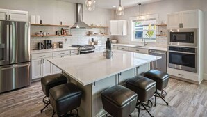 A modern kitchen with a large island, stainless steel appliances, and bar stools. - Family Home | Marina, Dover Bay | Extended Stays (Dover)