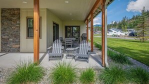 A covered outdoor seating area with Adirondack chairs and a table, a stone wall, and a view of a residential neighborhood. - Family Home | Marina, Dover Bay | Extended Stays (Dover)
