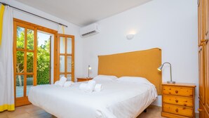 Ein Schlafzimmer mit einem großen Bett, einem hölzernen Kopfteil, einem Nachttisch mit Lampe und einem Fenster mit Vorhängen.