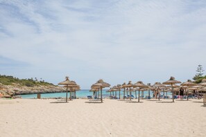 A beach with thatched umbrellas and lounge chairs.