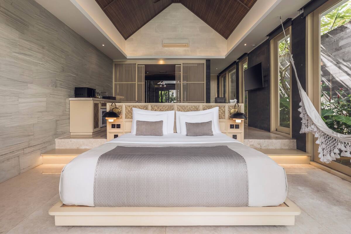 Ein modernes Schlafzimmer mit einem großen Bett, Nachttischen, einem Fernseher und Blick ins Freie.