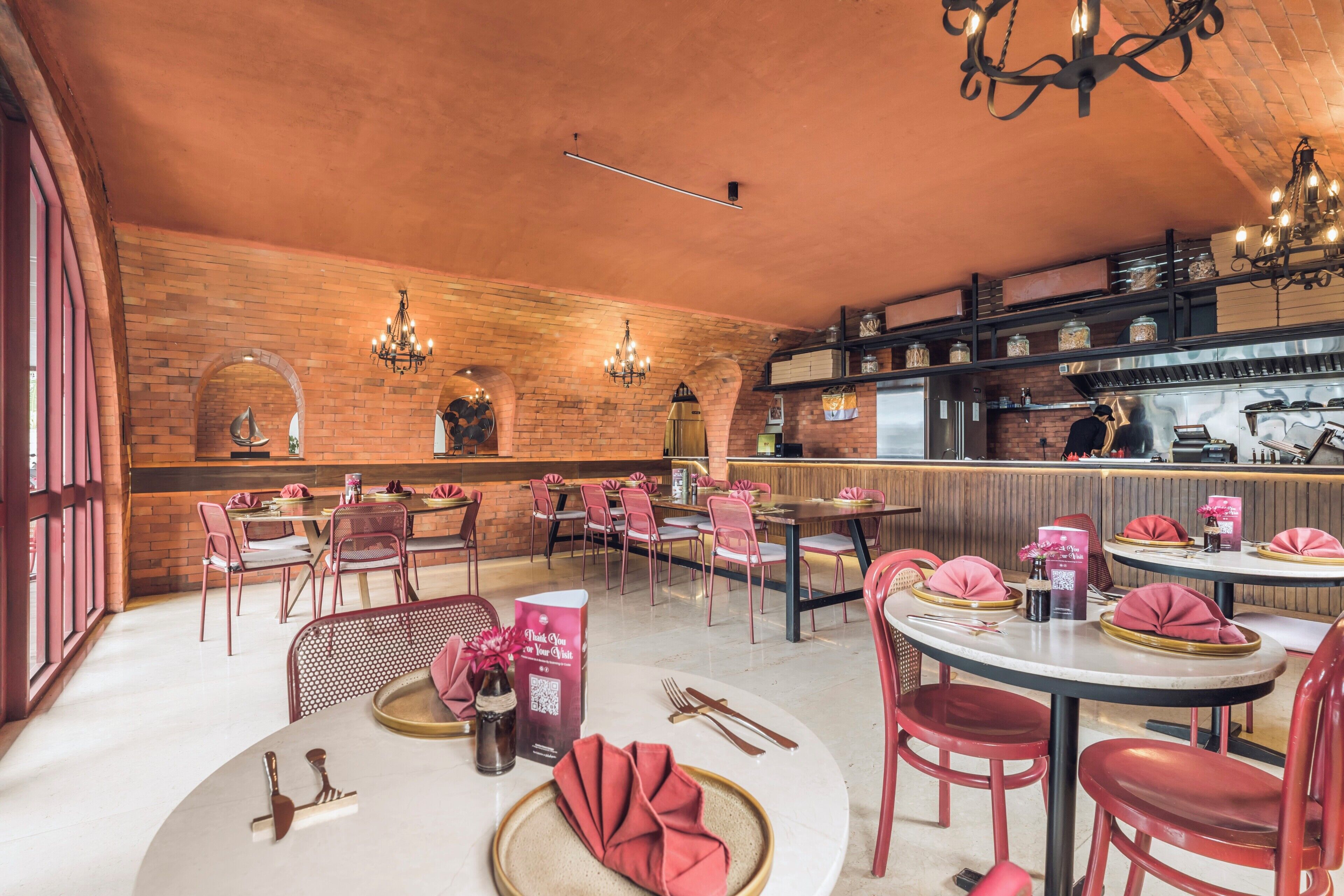 A restaurant with brick walls, round tables, and red chairs.