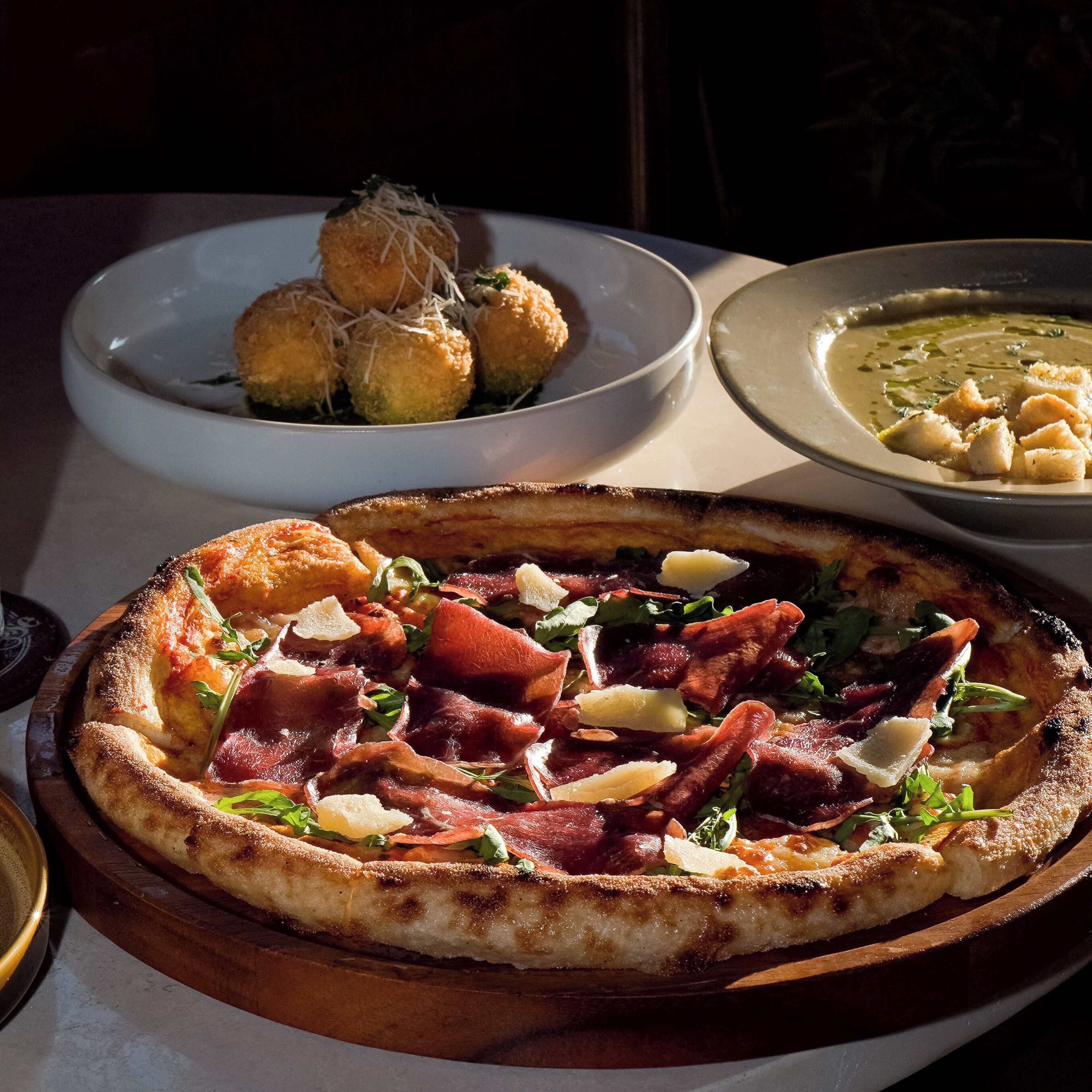 A pizza with various toppings, a bowl of soup, and a plate of breadsticks.