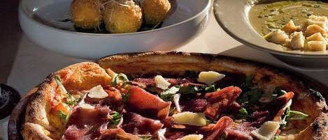 A pizza with various toppings, a bowl of soup, and a plate of breadsticks.