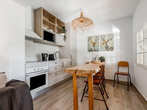 A modern kitchen with white cabinets, a wooden dining table, and a hanging light fixture.