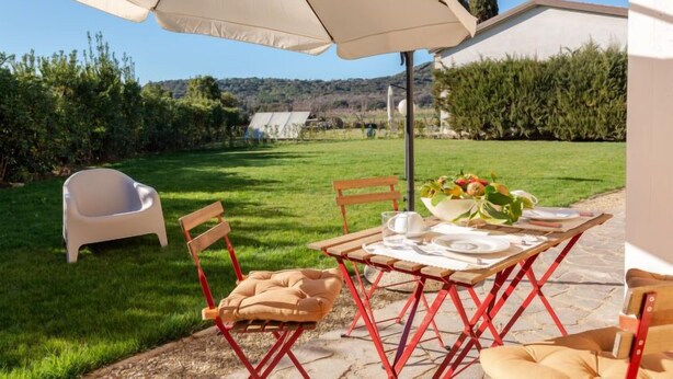A patio with a table set for two, a white plastic chair, and a beige cushion.