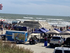 A beachside parking area with a food truck, tents, and a large rock formation with inscriptions.