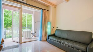 Un saló modern amb un sofà de pell negra, una porta de vidre que dona a un balcó i una taula petita amb cadires.