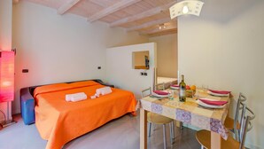 A bedroom with an orange bedspread, a bedside table with a bottle, and a dining area with a table set for two. - Orange Apartment Desenzano with Wi-fi & Balcony, Desenzano Del Garda, Italy (Desenzano Del Garda)