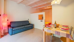 A room with a sofa, a dining table set with plates, glasses, and a bottle, and a ceiling with exposed beams. - Orange Apartment Desenzano with Wi-fi & Balcony, Desenzano Del Garda, Italy (Desenzano Del Garda)