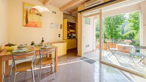 Un comedor con mesa y sillas de madera, una cocina con gabinetes amarillos y un balcón con mobiliario exterior.