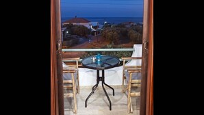 Un balcon avec une table et des chaises, donnant sur une zone côtière avec des maisons et de la végétation.