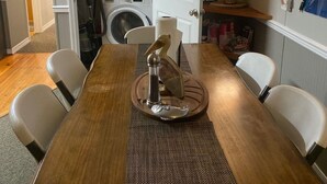 Ein Essbereich mit Holztisch, Stühlen und einem dekorativen Salzstreuer als Mittelpunkt. Im Hintergrund ist ein Waschraum mit Waschmaschine und Trockner erkennbar.