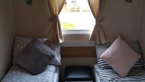 A small, compact room with two single beds, a bench, and a window with curtains. - 2 bedroom 6 berth  caravan with decking (Abergele)