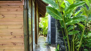 A wooden pathway leading to a building with a stone wall and lush green plants. - Private garden bungalow just 200m from the beach (Fare)