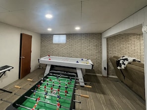 Una habitación con mesa de fútbol de mesa, un piano y una pared de ladrillo.