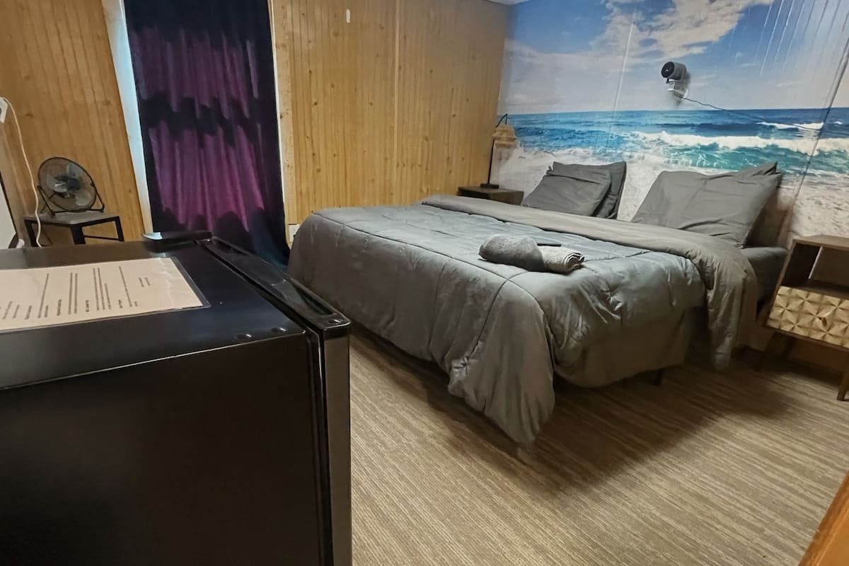 Un dormitorio con cama, escritorio, ventilador y un mural en la pared con vista al océano.