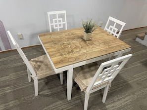 Una mesa cuadrada de madera con estampado floral, rodeada por cuatro sillas blancas con asientos acolchados.
