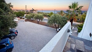A residential area with parked cars, a road, and a view of the sea at sunset. - Apartments with garden view, Creta, Ierapetra (Ierapetra)