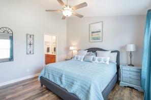 A bedroom with a bed, nightstands, a ceiling fan, a painting, and a mirror.